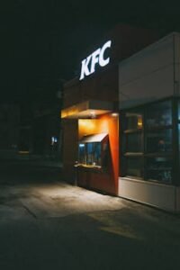 Capture of an illuminated KFC restaurant at night, featuring signage and a quiet street.
